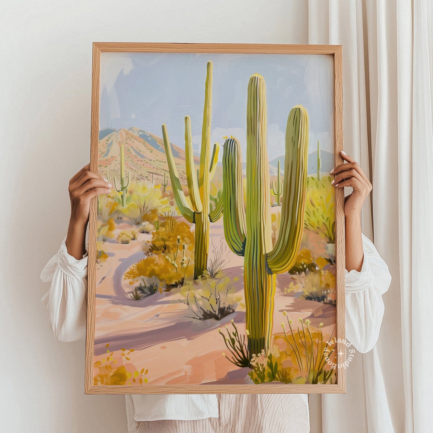 Person holding a framed painting of a desert landscape with cacti.