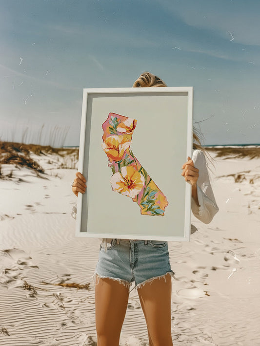 Person holding a framed floral map of California on a beach