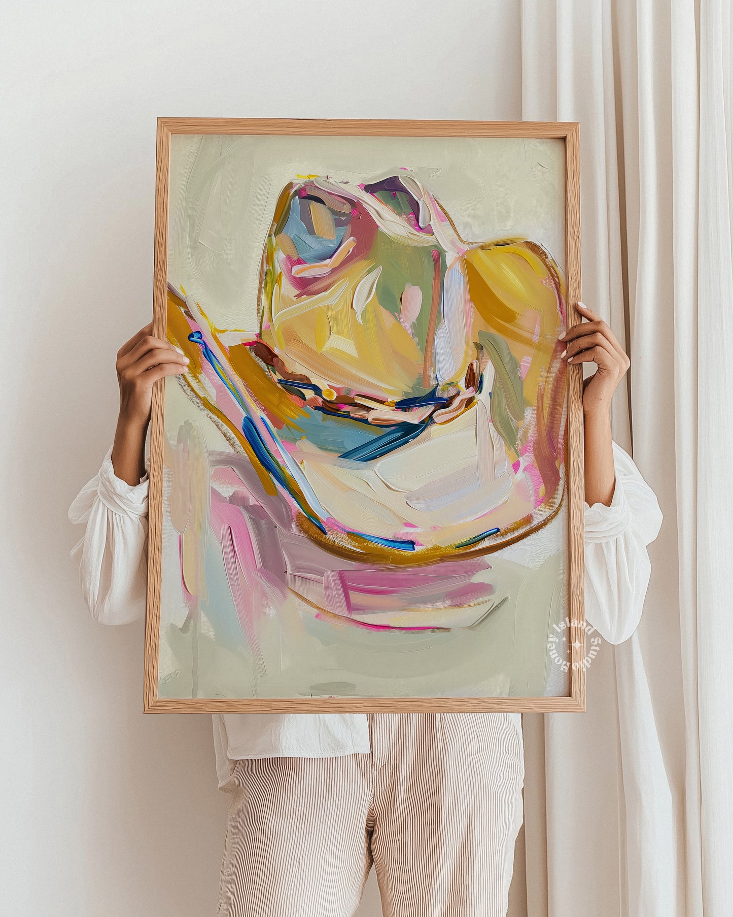Person holding a framed Cowgirl hat art print with colorful brushstrokes against a white wall.