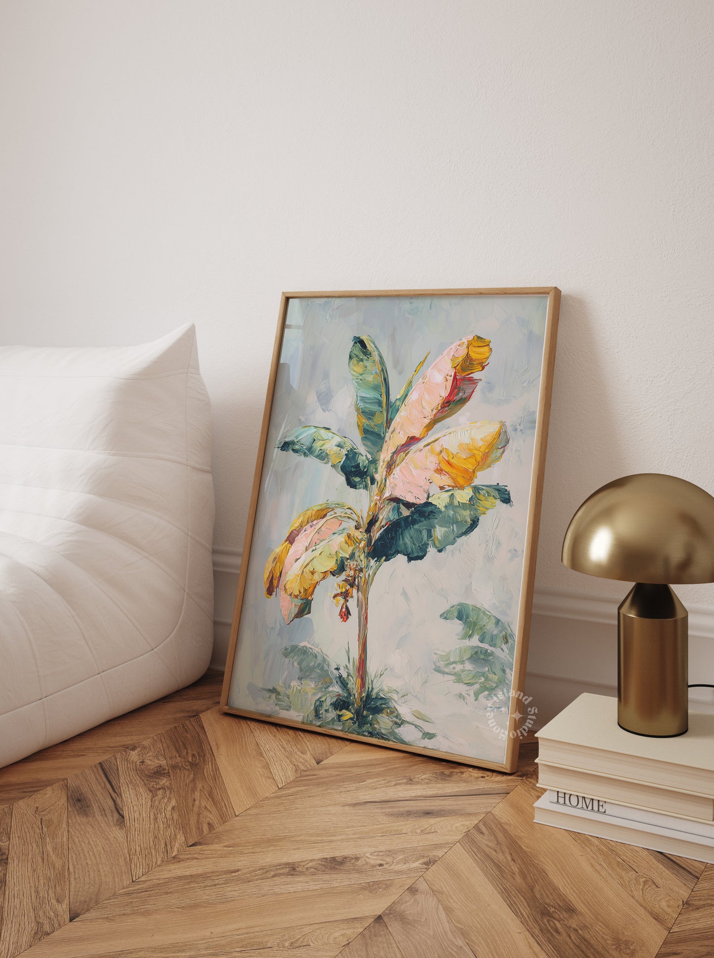 Framed floral artwork on a wall next to a gold lamp and books on a wooden floor.