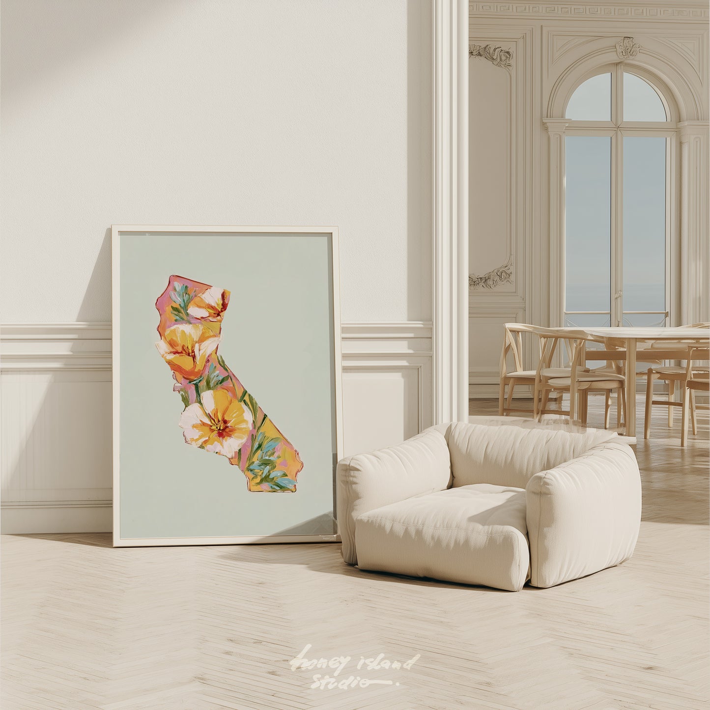Floral California map art print on a wall next to a beige armchair in a room with wooden flooring and a large window.