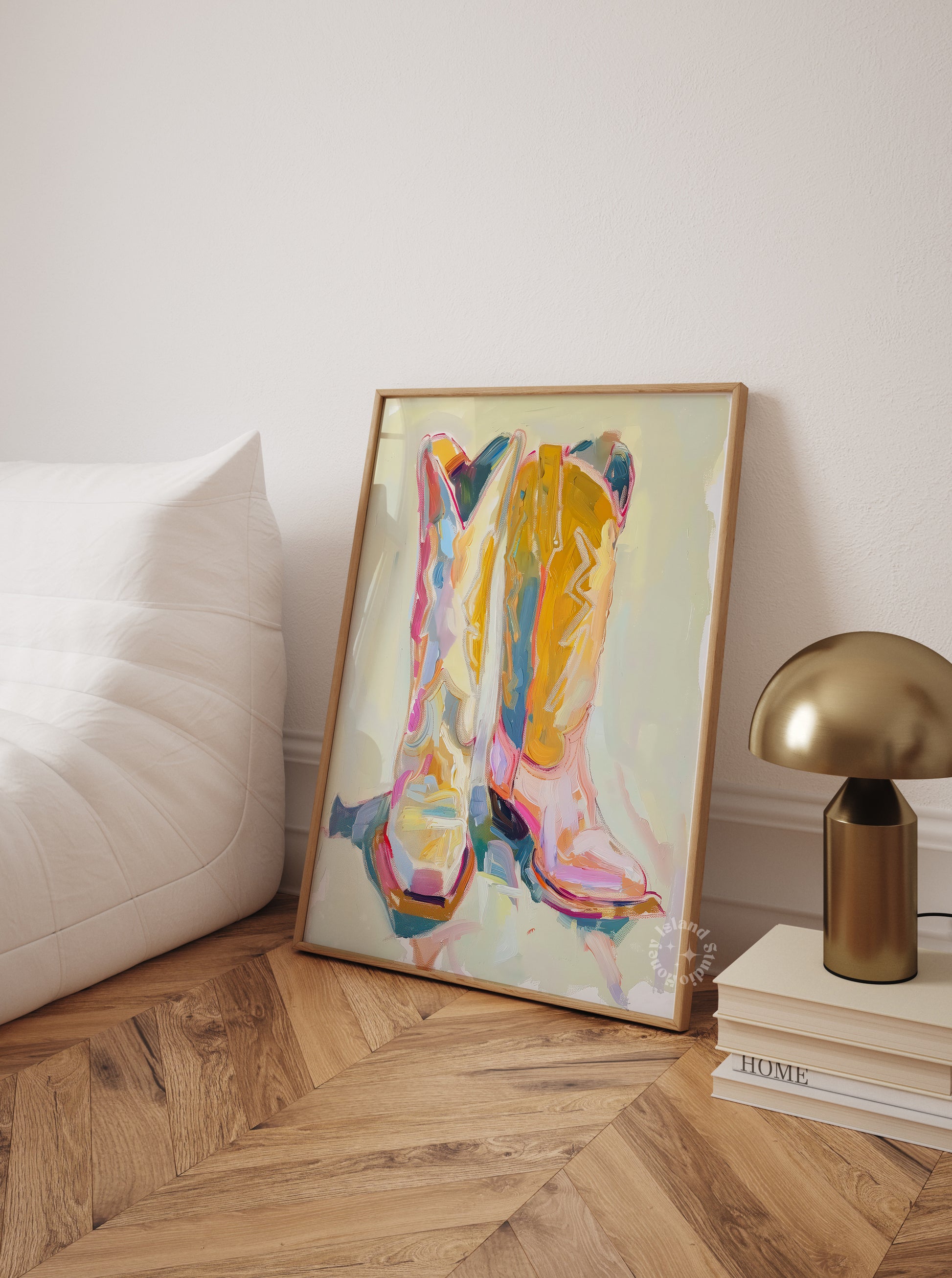 Framed western art piece on a wall next to a lamp and books on a wooden floor.