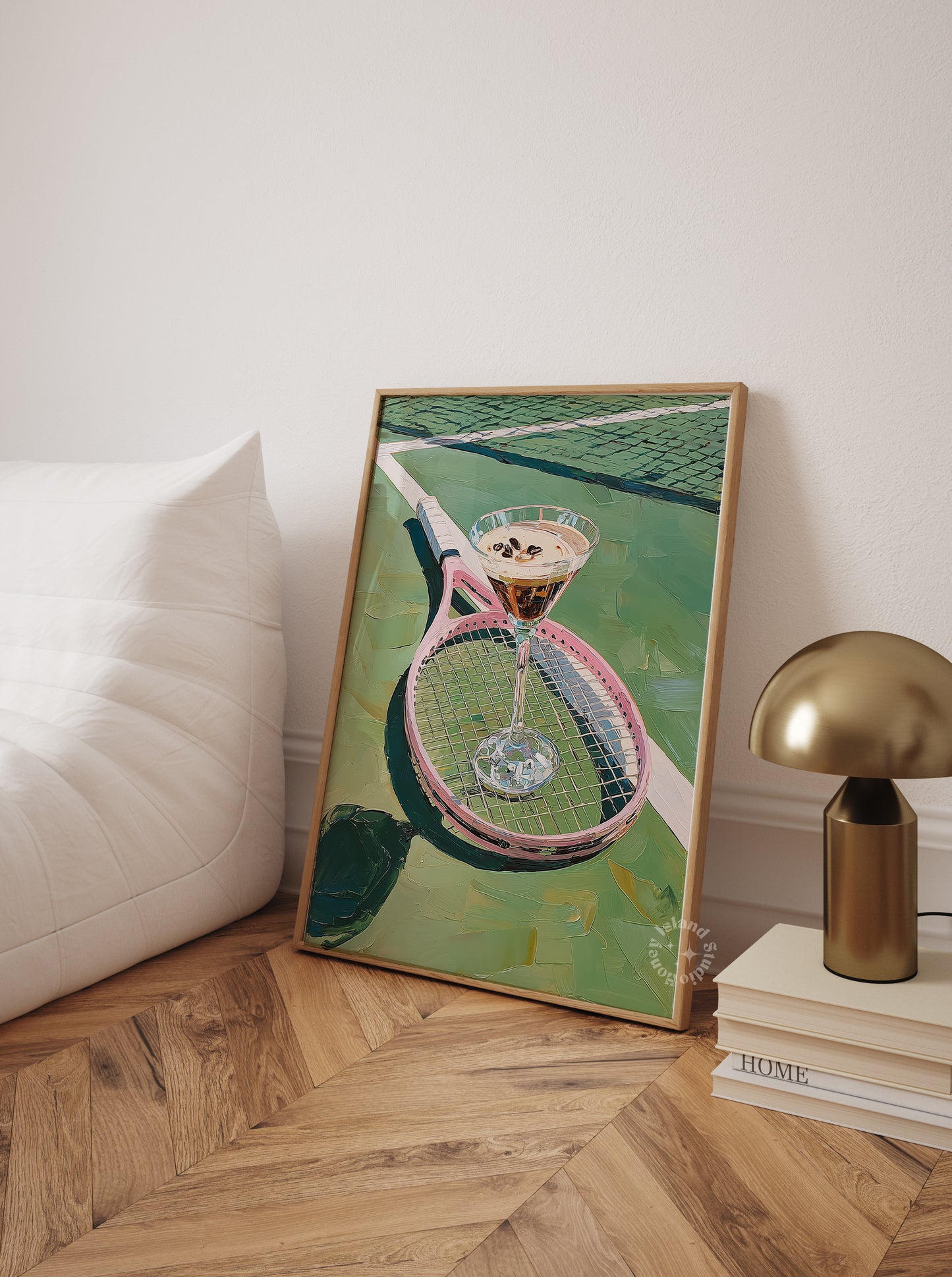 Framed artwork of a tennis racket and ball on a wall next to a lamp and books.