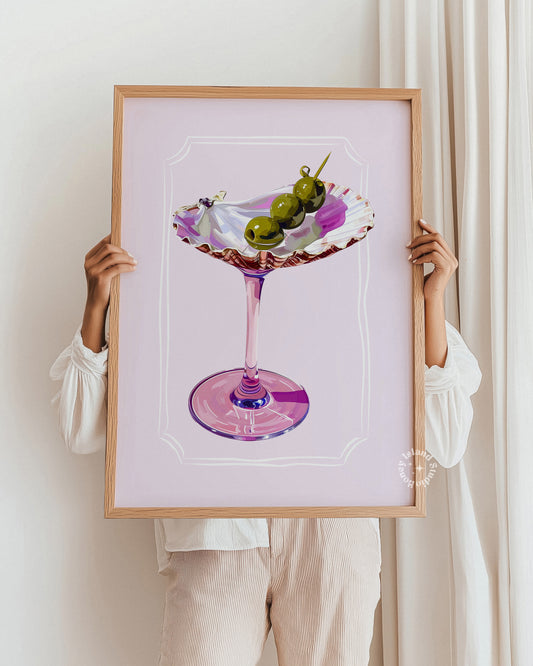 Framed artwork of a cocktail with olives held by a person against a white background
