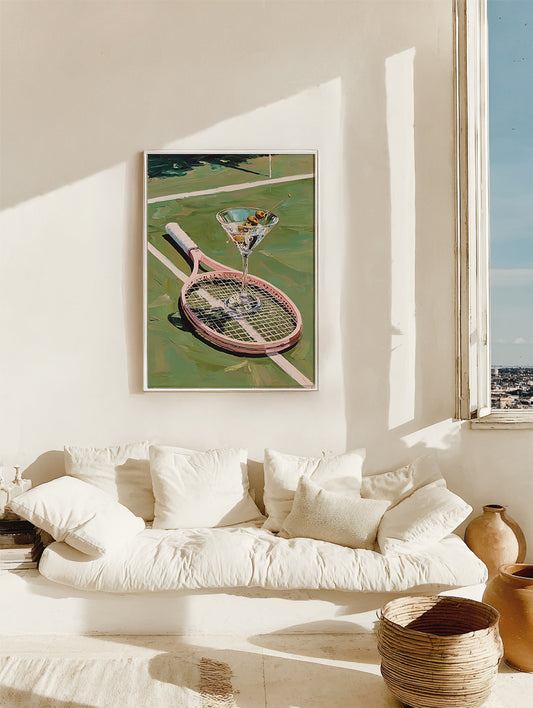 Framed artwork of a pink tennis racket with a martini glass on a tennis court, displayed in a living room.
