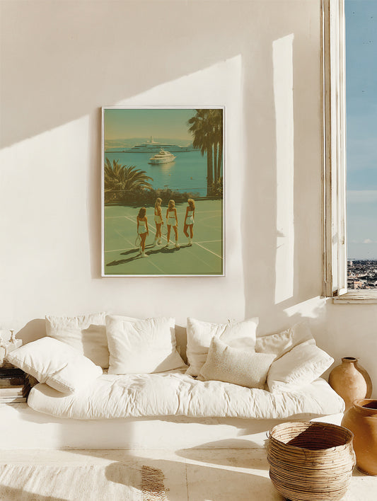 Framed artwork of three women on a tennis court with a scenic view, hanging above a white sofa in a bright room.