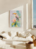 Framed artwork of a toucan on a flower in a living room with a white sofa and window view.