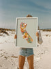 Person holding a framed floral map of California on a beach