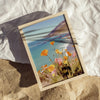 Framed artwork of a beach scene with flowers on a the sand on the beach