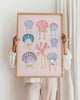 Framed artwork with colorful shell and bow illustrations held by a person.