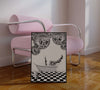a framed black white poster whosing disco balls champagne and  bathtub styles against a pink chair