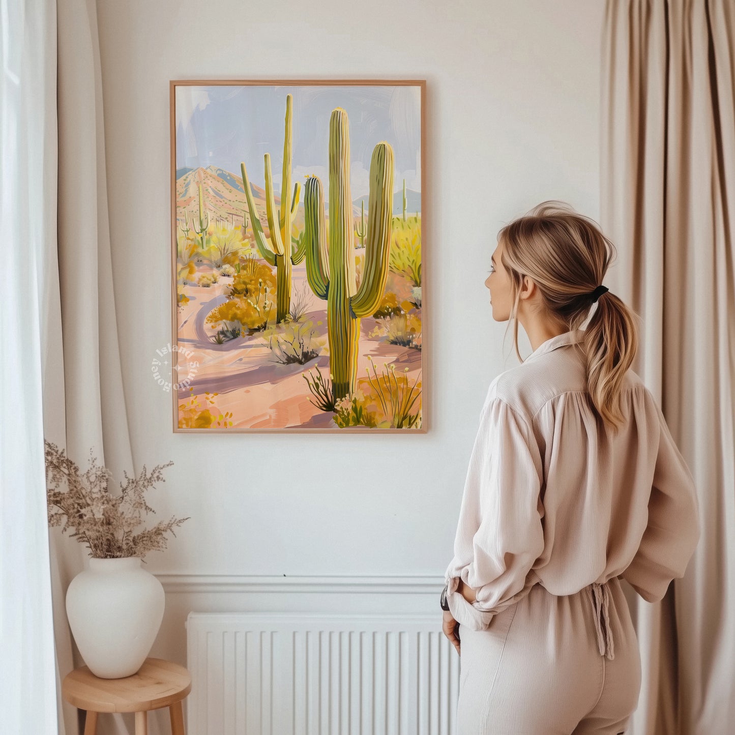 Woman standing in a room looking at a painting of cacti on the wall.