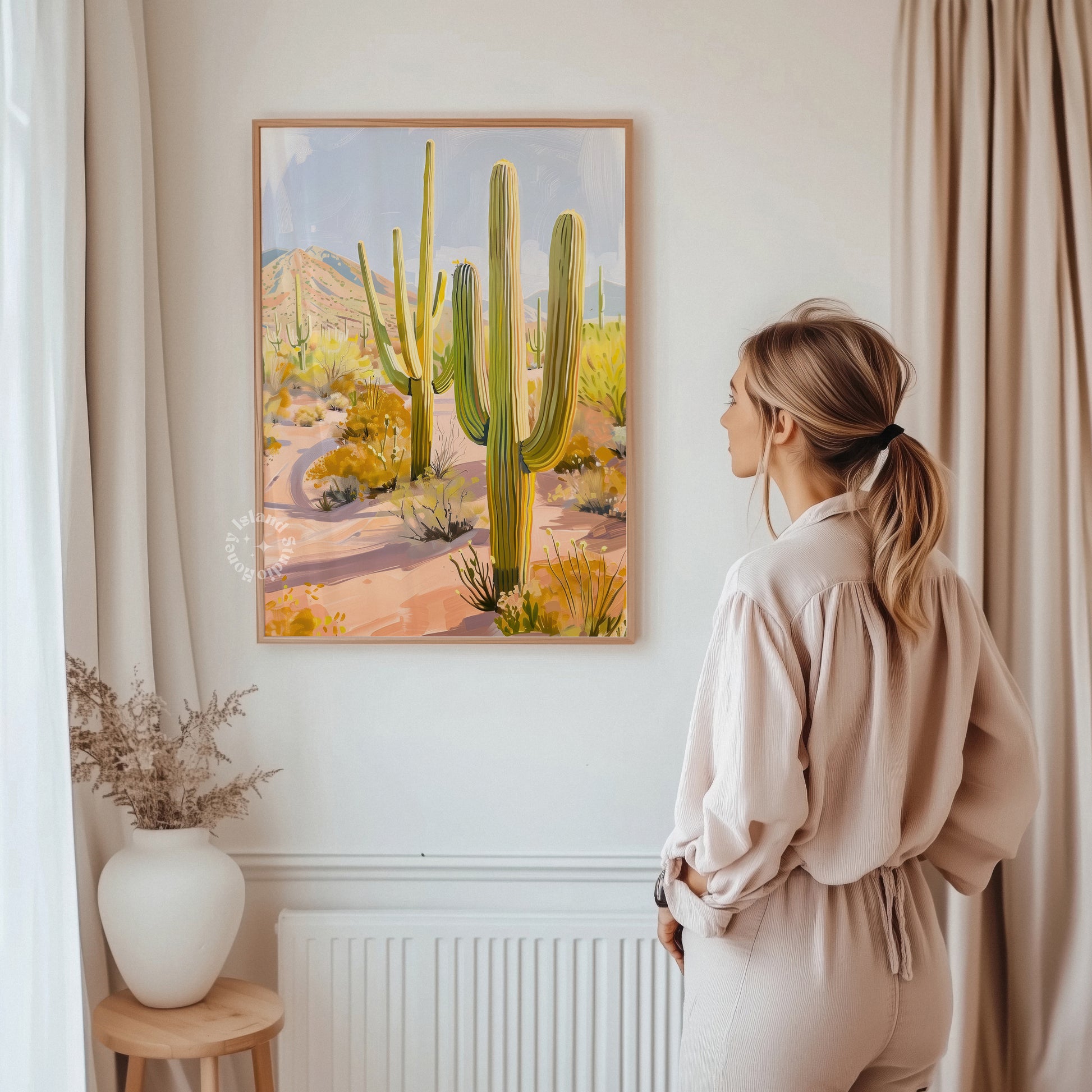Woman standing in a room looking at a painting of cacti on the wall.