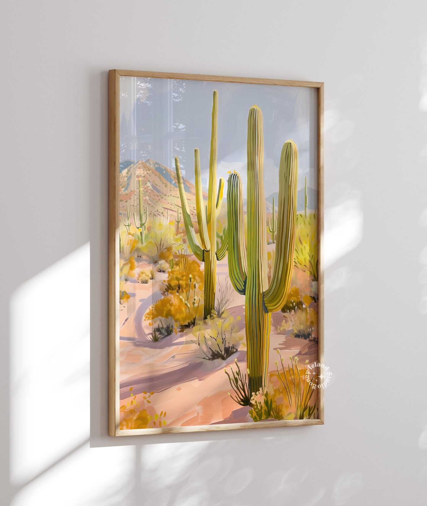 Framed artwork of a desert landscape with cacti on a white wall