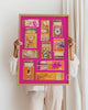 Person holding a framed artwork with matchbox art on a pink background