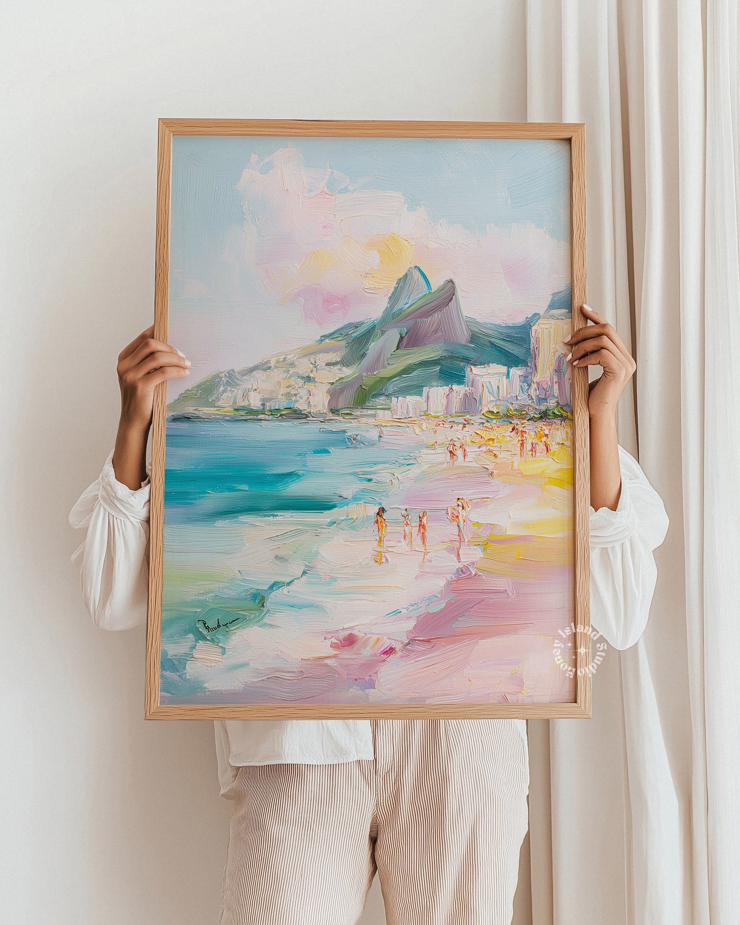 Person holding a framed watercolor painting of a beach scene with mountains.
