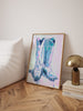 Framed abstract art piece on a side table with a lamp and books in a room.