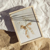 Framed artwork with a plant and bow on a textured surface
