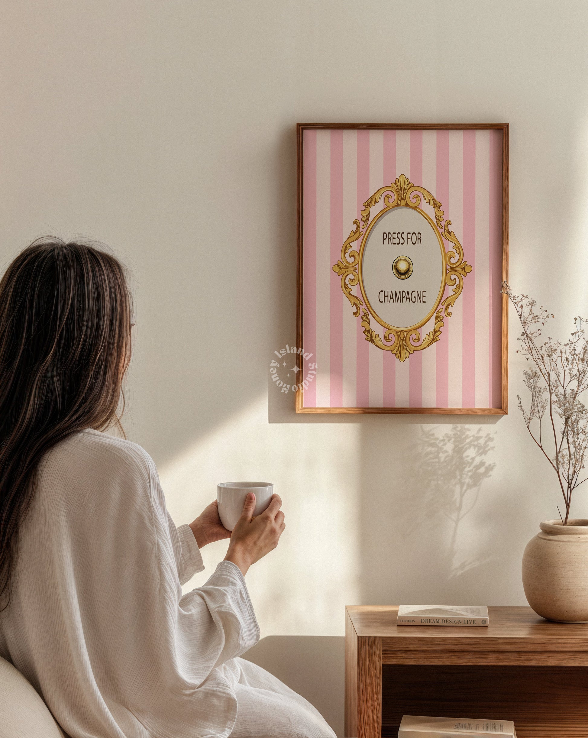 Woman in a white robe holding a cup, sitting in front of a decorative wall art piece.