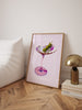 Framed artwork of a cocktail glass on a wooden floor with a lamp and books in the background.