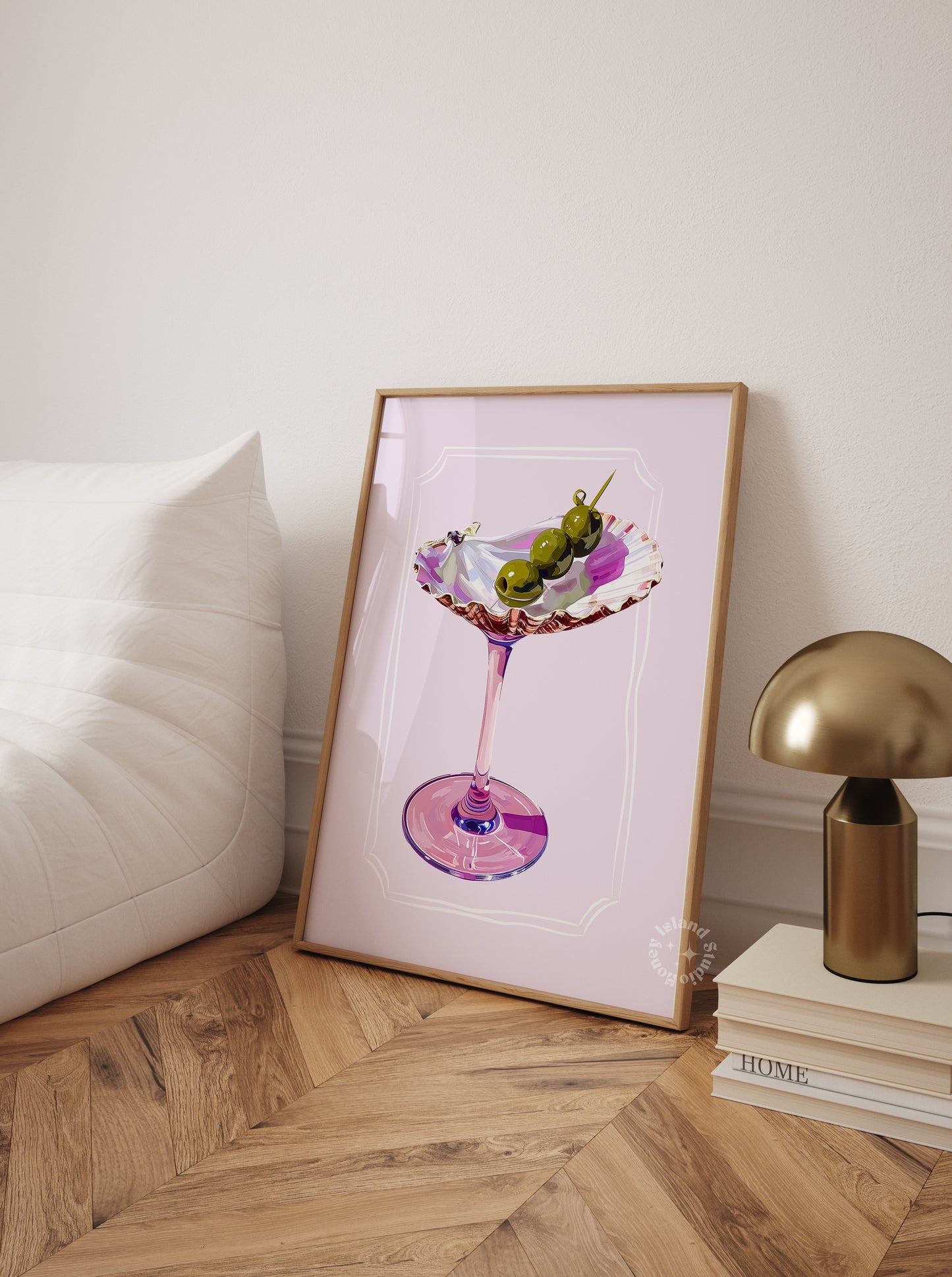 Framed artwork of a cocktail glass on a wooden floor with a lamp and books in the background.