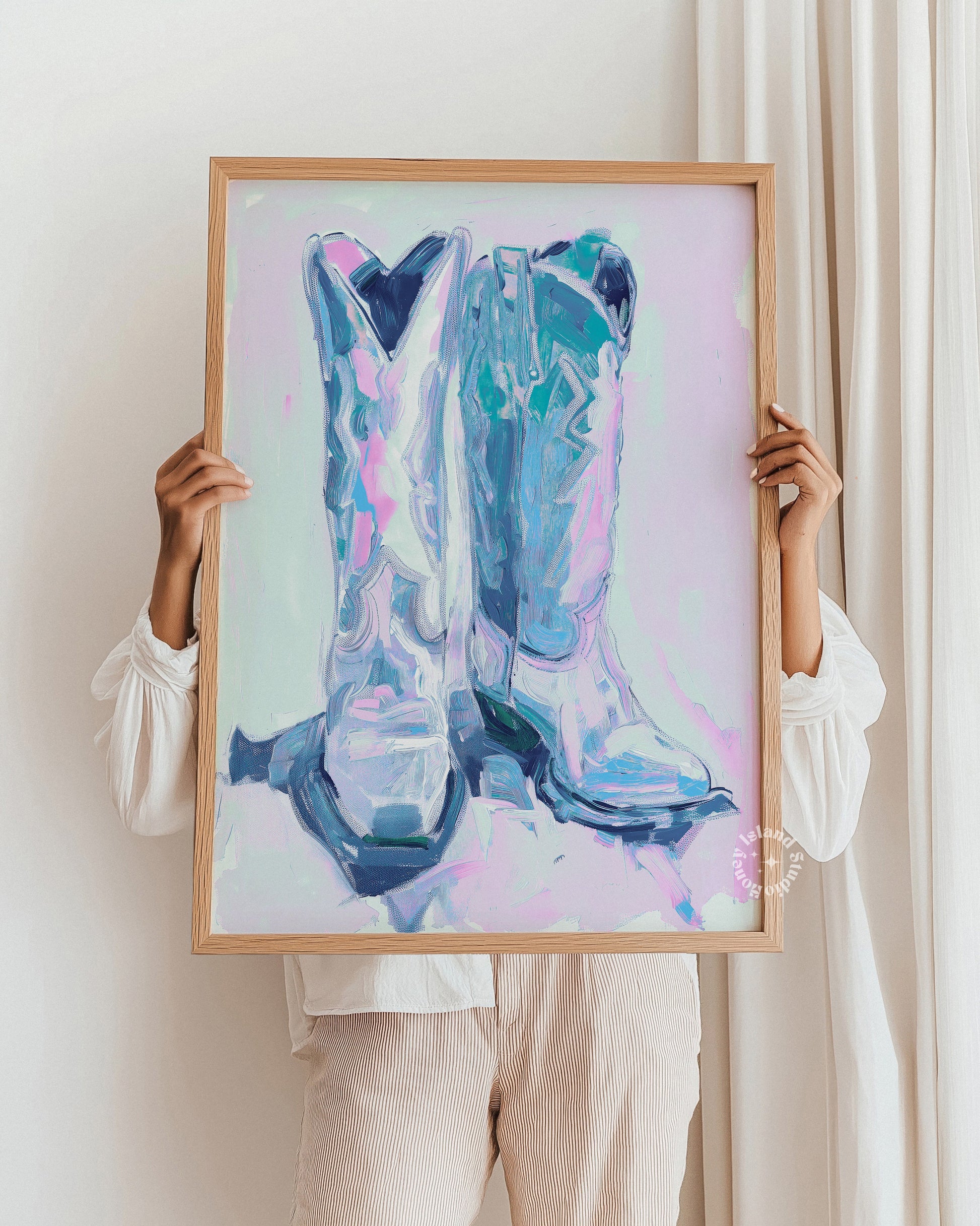 Person holding a framed painting of blue cowboy boots against a white background
