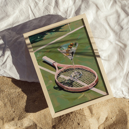 Framed artwork of a martini glass on a tennis racket with a beach setting