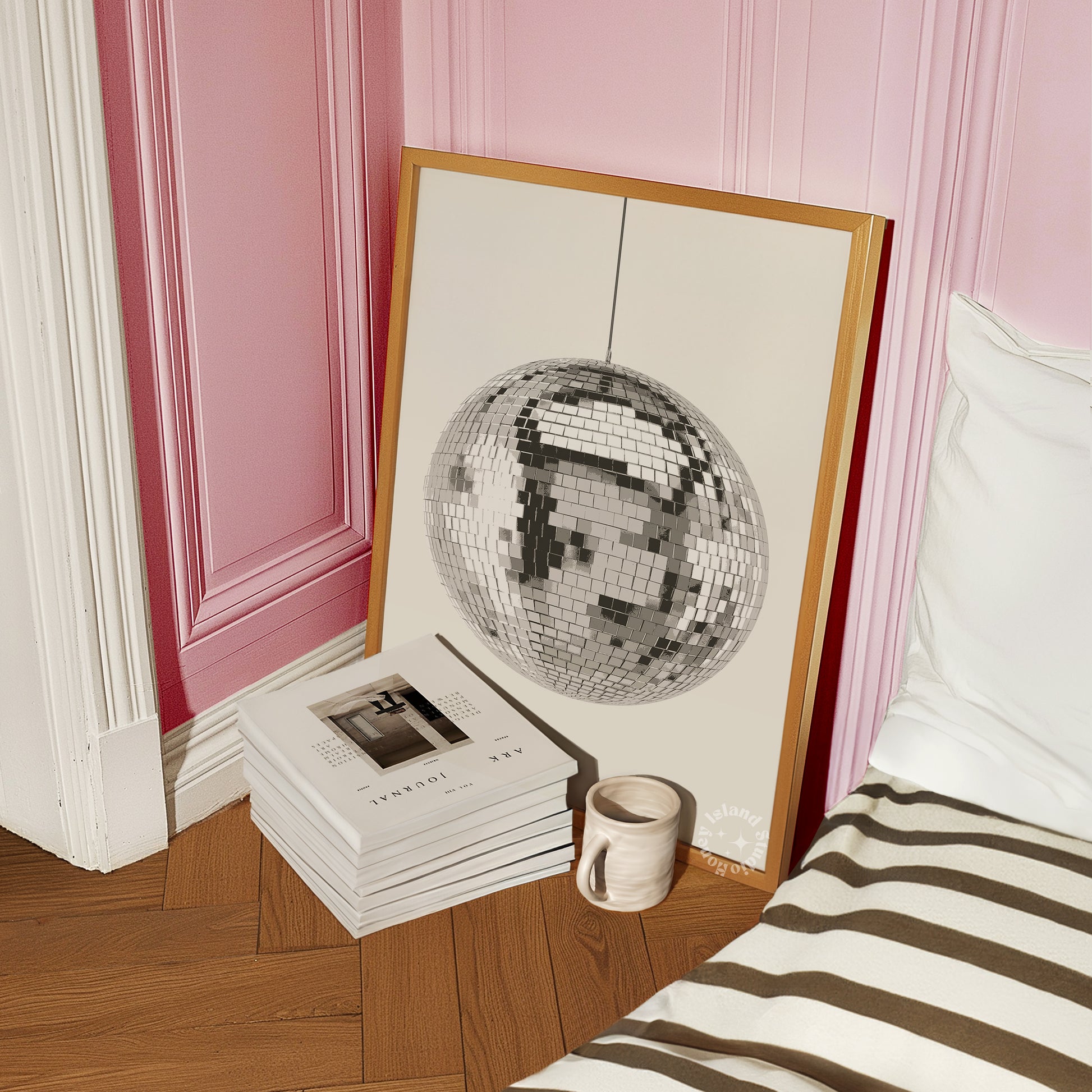 disco ball wall art framed in the floor of a bedroom next to books and mug