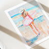 Framed watercolor painting of a woman in a swimsuit on a beach.