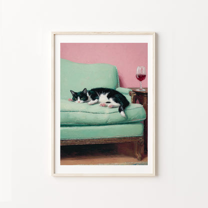 Framed artwork of a cat lying on a green couch with a pink wall in the background.