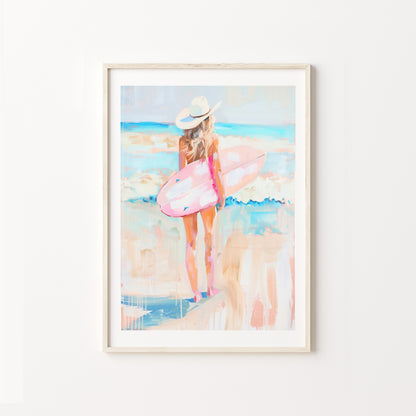 Framed artwork of a woman with a pink surfboard on a beach.