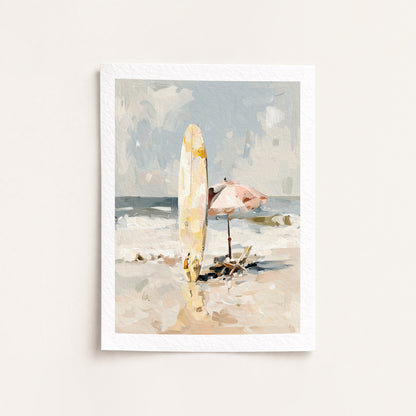 Framed artwork of a beach scene with a surfboard and umbrella on a white wall.