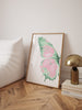 Framed butterfly artwork on a wall next to a lamp and books on a wooden floor.