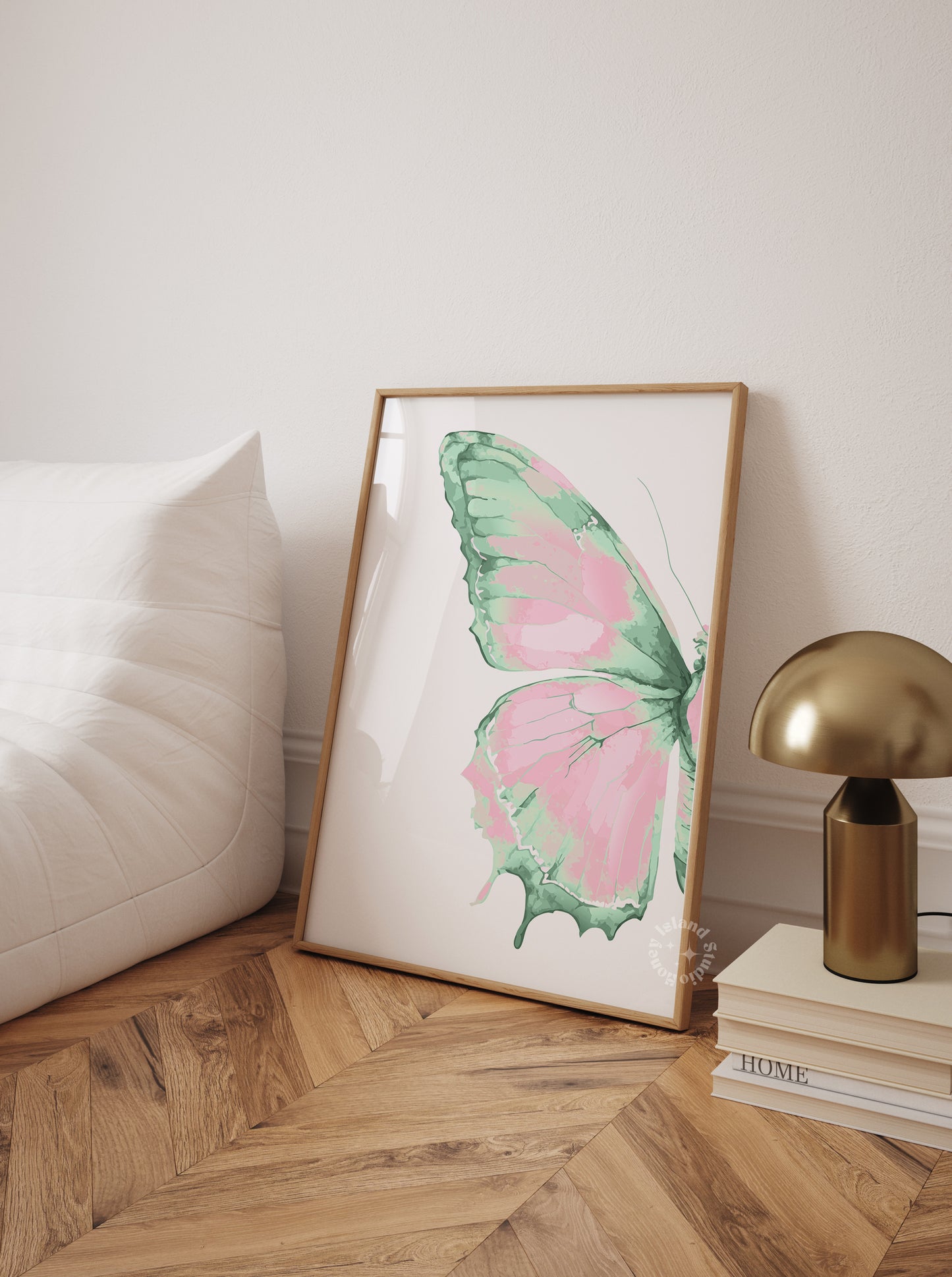 Framed butterfly artwork on a wall next to a lamp and books on a wooden floor.