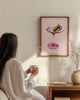 Woman in a white robe holding a mug, sitting in a room with a framed artwork of a cocktail on the wall.