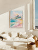 Framed artwork of a coastal scene above a white sofa in a bright room with a window.