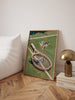 Framed artwork of a tennis racket with a martini glass on a green background, placed on a wooden floor.