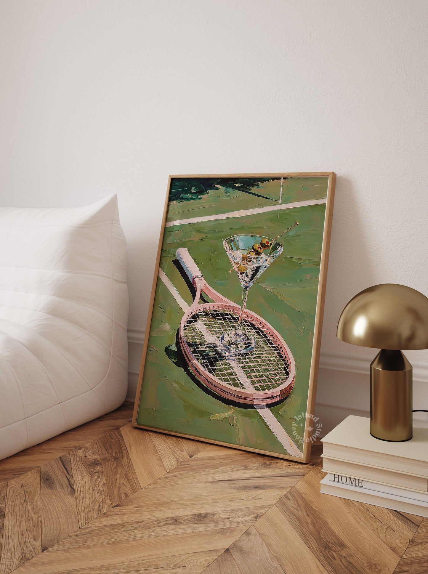Framed artwork of a tennis racket with a martini glass on a green background, placed on a wooden floor.