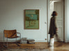 Brown leather chair and stack of books in a room with a painting on the wall.