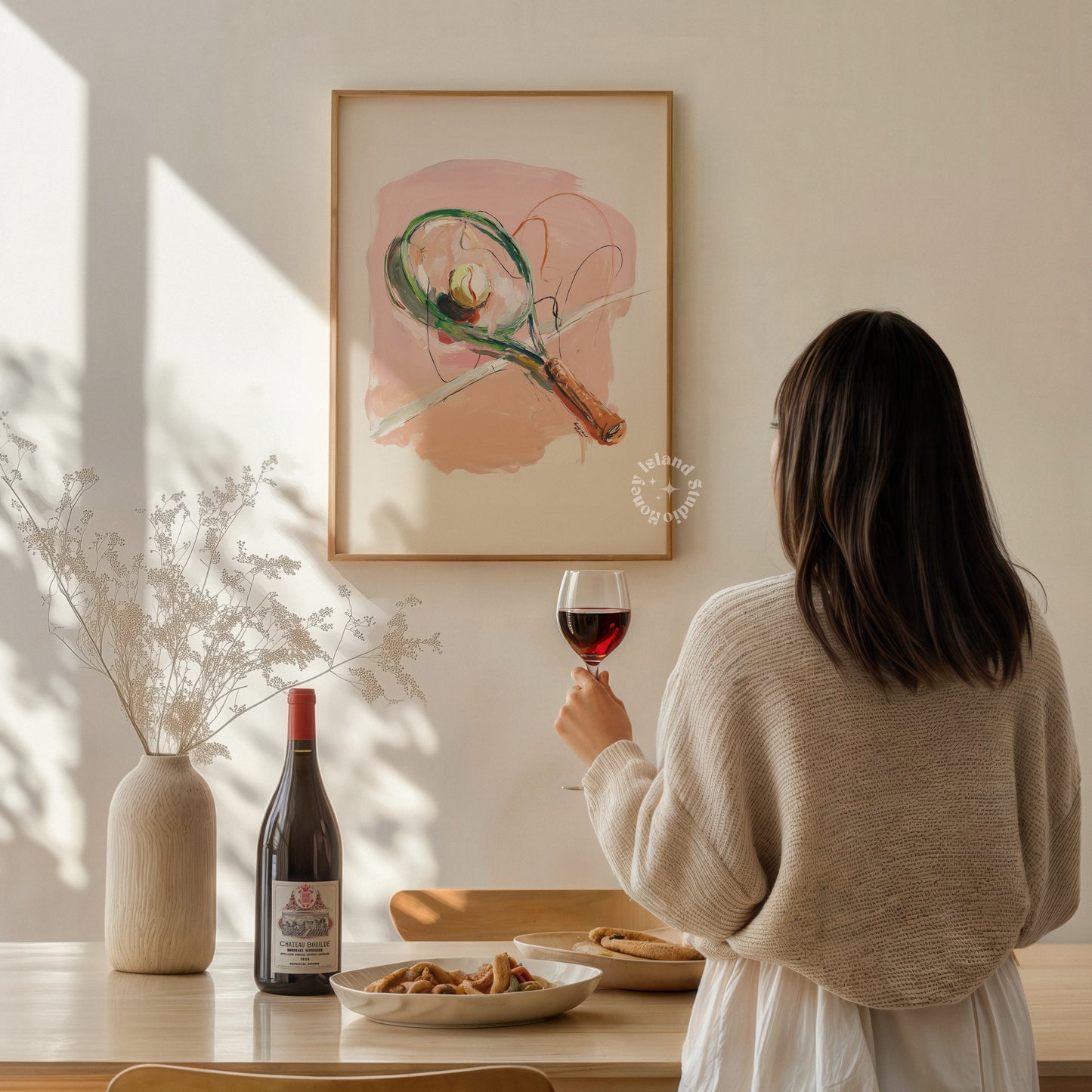 Woman holding a glass of red wine in a cozy room with a painting on the wall.