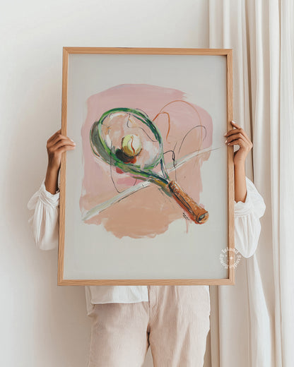 Person holding a framed abstract painting of a tennis racket against a white wall.
