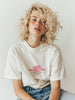 Person wearing a white t-shirt with a graphic design on a plain background