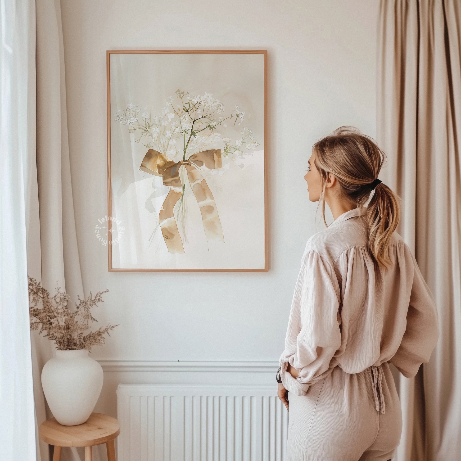 Woman standing in a room with a framed artwork on the wall, a vase with plants on a small table, and beige curtains.