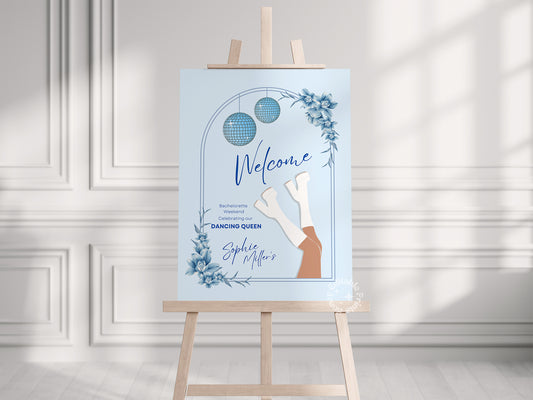 Light blue Mamma Mia-themed welcome sign for a bachelorette weekend party, elegantly displayed on an easel in a sunlit room with a white wall background. The sign features a Mediterranean-inspired design, perfect for a fun and stylish celebration.